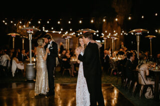 Bride and groom dancing with their parents while guests watch