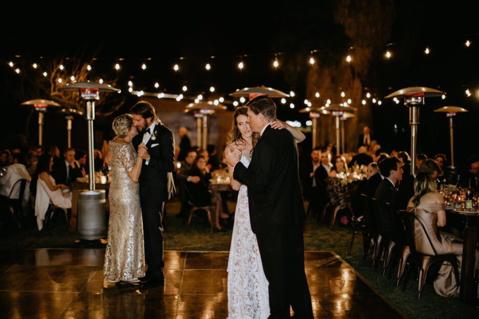 Bride and groom dancing with their parents while guests watch