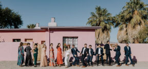 Wedding party acting silly for photographer outside of pink adobe building